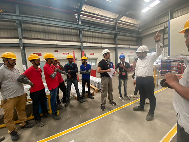 Briefing a line of workers in hard hats on a factory floor